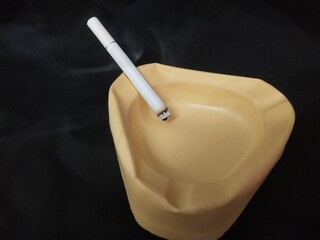
yellow ceramic cigarette ashtray and a menthol white cigarette close-up on black background. photo taken in malaysia