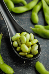 Green edamame pods. Fresh soybeans on ceramic spoon on black table.