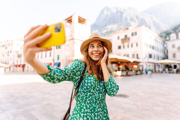 Fototapeta premium Happy woman takes a selfie photo on a smartphone against the background of old city. Travel and life in Italy.