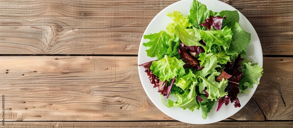 Aufkleber Top view of a salad with crisp lettuce leaves in a white plate on a wooden table background featuring copy space image