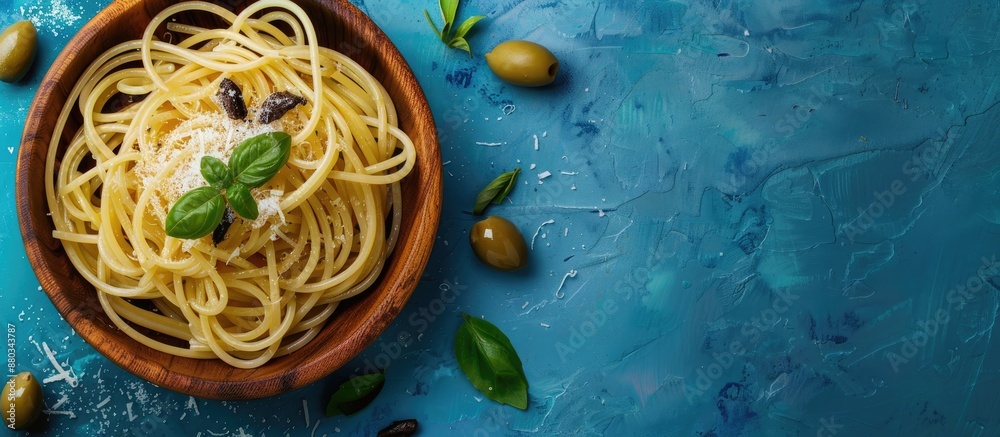 Poster an italian plate of anchovy spaghetti with salt in a wooden bowl and olives on a blue texture backgr
