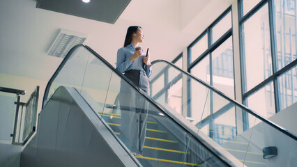A business woman is walking down to escalator with a coffee cup in her hand