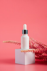 Plastic white tube for cream or lotion. Skin care or sunscreen cosmetic with fake flowers on pink background.