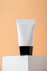 Plastic white tube for cream or lotion. Skin care or sunscreen cosmetic with stylish props on cream background.