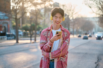 Young Asian guy with headphones listening to music outdoors