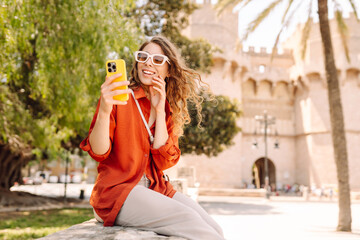 Happy woman tourist walking through the European street outdoors and making selfie. Travel, tourism, technology, blogging, communication concept.