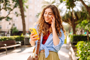 Obraz premium Woman traveler with a mobile phone on the street city. Young Woman texting, browsing, using her smartphone on a warm sunny day. Business, technology, blogging, communication concept.