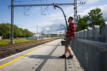 A European-looking man in sunglasses waits for a train on the platform on a summer day in Tallinn.