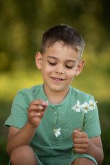 pre-schoolar boy with chamomile at green nature field on sunset time 