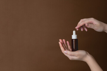 Hand holding serum glass bottle or essential oil on brown background. Natural Organic Spa Cosmetic concept