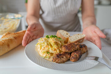 Woman serving a homemade cooked meal with pan fried cevapcici, coleslaw and bread on a plate