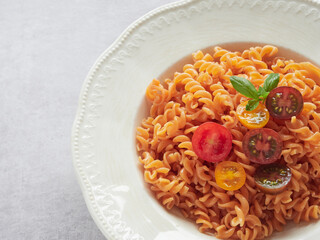 close-up view plate with pasta spirals (fussili) of red lentils with colorful cherry tomatoes and fresh basil leaves