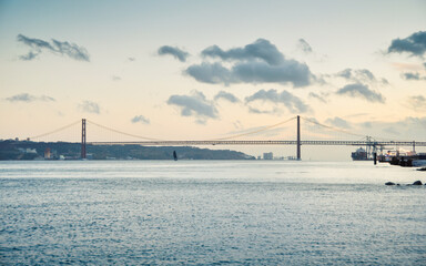 Tagus estuary bay at dusk. Sky partially covered with clouds. Silhouette of 25 de Abril Bridge between Lisbon and Almada in the background. 