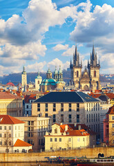 Naklejka premium High spires towers of Tyn church in Prague city (Church Our Lady before cathedral) urban landscape panorama with red roofs houses old town and blue sky clouds
