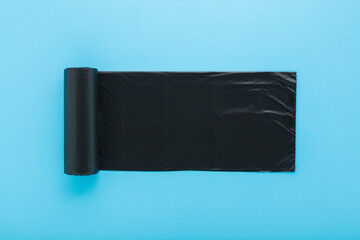 New dark black roll of plastic garbage bag on light blue table background. Pastel color. Closeup. Top down view.
