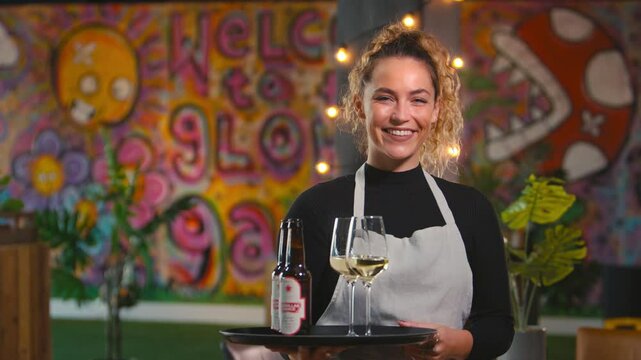 Portrait of smiling female server holding tray of drinks in cool bar or club - shot in slow motion