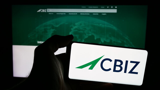 Stuttgart, Germany - 07-06-2024: Person holding smartphone with logo of US financial consulting company CBIZ Inc. in front of website. Focus on phone display.