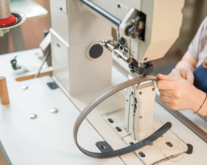 A woman tanner sews a leather belt on a sewing machine. Close-up of hands.