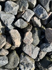 A close-up view of varied stones, illuminated by sunlight. The grey and pink-hued rocks showcases their unique textures and patterns, creating a visually striking natural mosaic