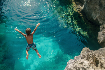 Fototapeta premium Exhilarating Plunge: Kid Diving into Crystal Clear Blue Natural Pool from Above