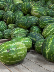 Fresh organic watermelons at the farmer's market, watermelons in close-up. There are a lot of whole watermelons on the wooden floor. 