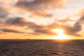 Antarctica Beautiful Sunset Clouds Over Ocean with Icebergs in the Distance. Glorious Golden Light Colorful Sky Scenic Sailing Landscape