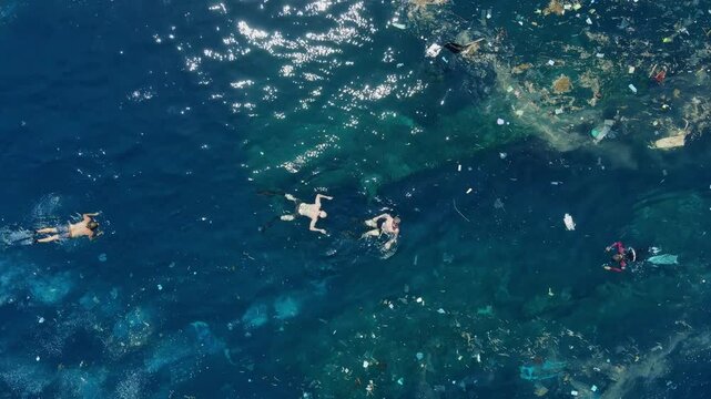 People swimming in dirty ocean with plastic pollution in Bali.