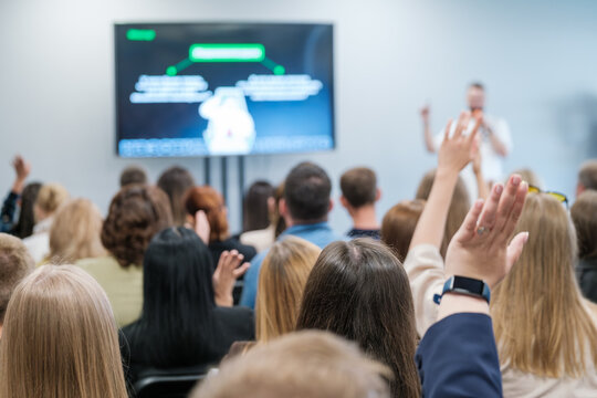 Engaged audience raising hands in a business presentation, indicating active participation and an interactive Q&A session. Ideal for concepts of learning, teamwork, and seminars.