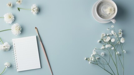 Obraz premium Flat lay of white flowers, a notebook, and a coffee cup on a blue background. Perfect for stationary, floral, or relaxation themes.