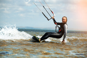 Smiling woman with a kiteboard looks at the camera while sailing through the waves on a parachute, kite. Fast travel with a wave from the board