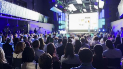 Large audience attending a business presentation in a modern conference hall with vibrant lighting and big screen.