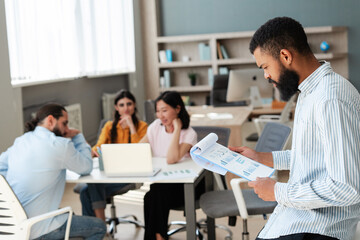 Obraz premium Focused businessman analyzing charts while colleagues collaborate in modern office