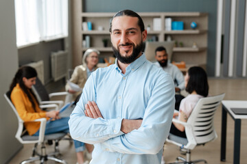 Confident businessman smiling with arms crossed in office meeting. Successful business concept