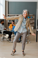 Happy senior businesswoman dancing in office with colleagues watching