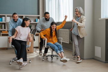 Happy office workers having fun riding on chairs in modern office