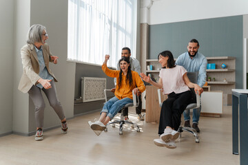 Happy business team having fun racing on chairs in office