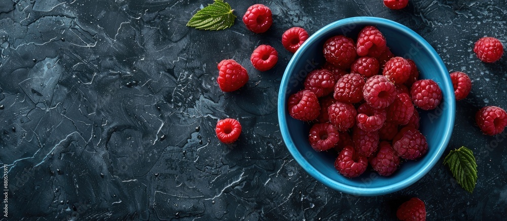 Poster top down view of ripe raspberries in a blue bowl on a rugged black backdrop with space for text or i