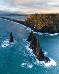 Aerial view of the Reynisdrangar sea stacks along the south coast of Iceland, with dramatic cliffs and ocean waves. © _mishamartin