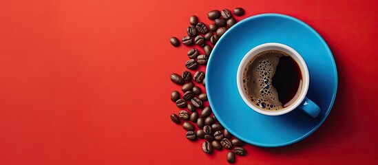 Top view of a blue cup of coffee with roasted coffee beans on a saucer against a red background offering copy space image