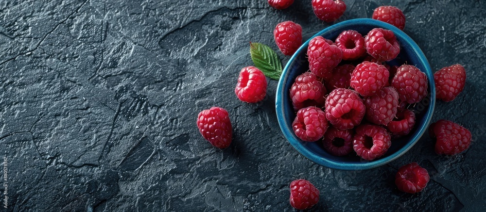 Poster top down view of ripe raspberries in a blue bowl on a rugged black backdrop with space for text or i