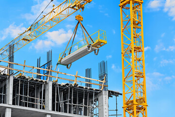 Vibrant yellow crane lifting concrete slabs at high rise building construction site against blue sky background