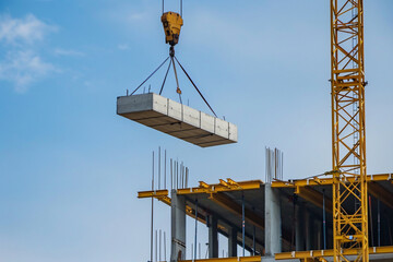 Vibrant yellow crane lifting concrete slabs at high rise building construction site against blue sky background