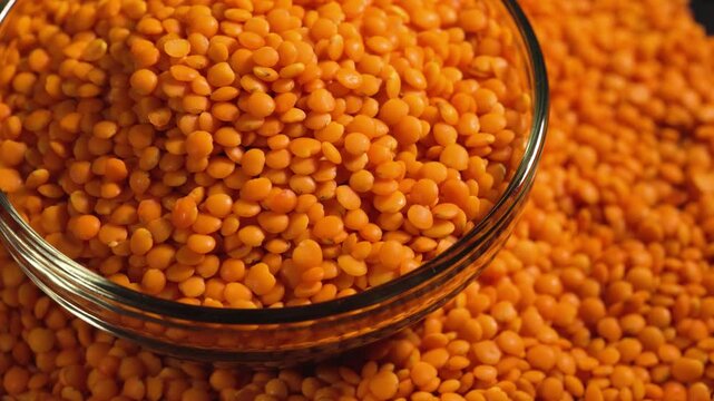 Raw red lentils are scattered out of the glass bowl.