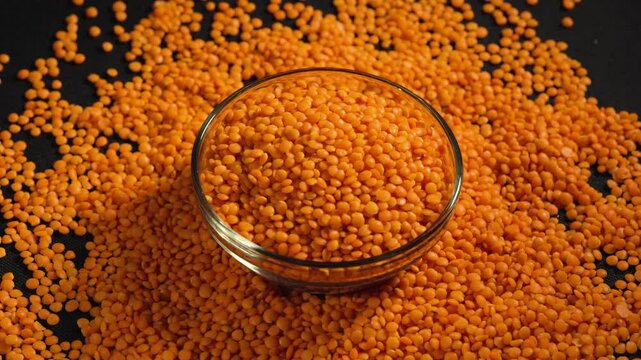 Raw red lentils are scattered out of the glass bowl.