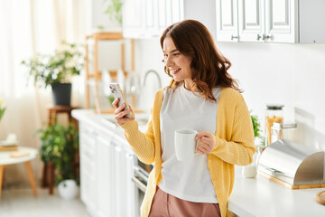 Middle-aged woman stands in kitchen, engrossed in cell phone.