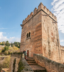 Adult mother with sunglasses and her daughter aside a castle tower entrance in Alhambra gardens. Enjoying the view of Granada city, Spain. Wearing winter clothes on a sunny day. Traveling outdoors.