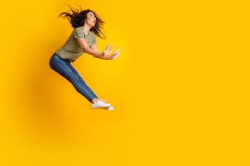Full size photo of astonished crazy girl dressed striped t-shirt jeans flying look at sale empty space isolated on yellow color background