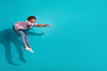 Photo of positive crazy man wear trendy striped clothes fly air empty space isolated on cyan color background