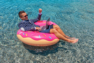 Businessman using laptop computer on an inflatable donut in the sea. Summer vacation concept.