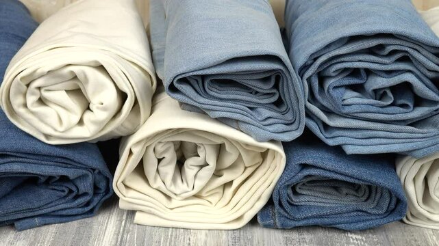 Trendy folded into a roll blue, white and black jeans are stacked on a gray wooden table, background